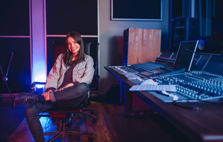 89713102-happy-young-woman-sitting-in-sound-recording-studio-female-music-composer-sitting-by-sound-mixing-co